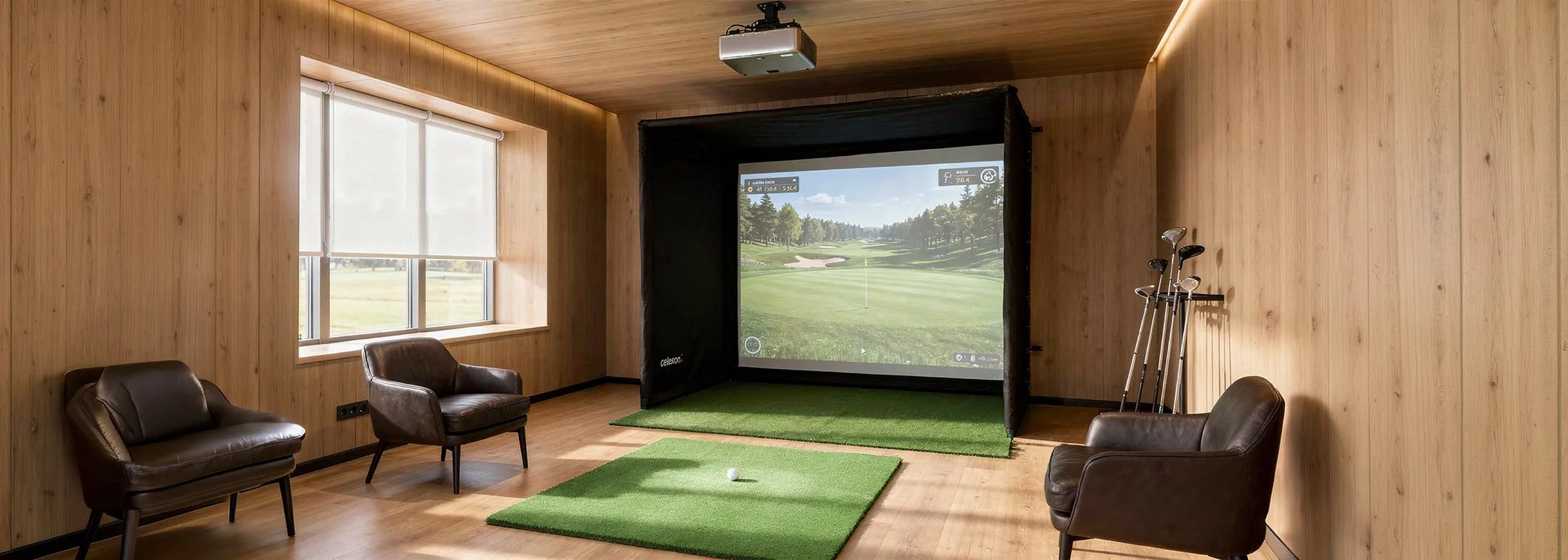 The image shows a stylish indoor golf simulator in a modernly furnished room with warm wood paneling. In front of a large projection screen inside a black simulation enclosure lies an artificial turf mat with a golf ball ready, while a projector mounted on the ceiling projects the virtual golf game onto the screen. Several golf clubs stand next to the setup, and two comfortable leather armchairs as well as large windows with a view outside complete the scene.