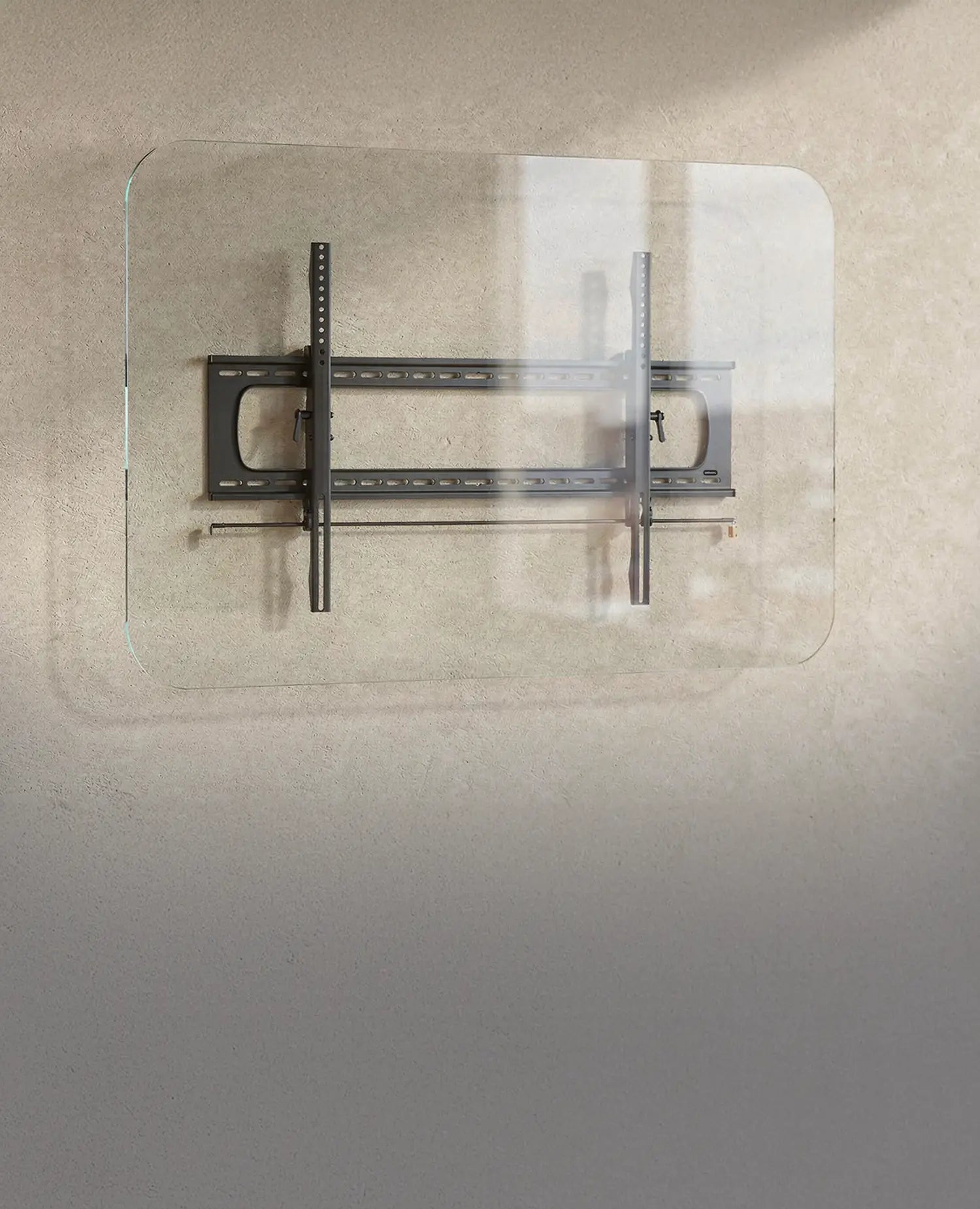 The image shows the celexon TV/display wall mount Adjust/Fixed attached to a transparent glass panel. The bracket consists of a sturdy metal construction with horizontal and vertical rails for mounting a screen. The scene is set in a modern office or workspace with a neutral wall, large windows, and a desk in the background.