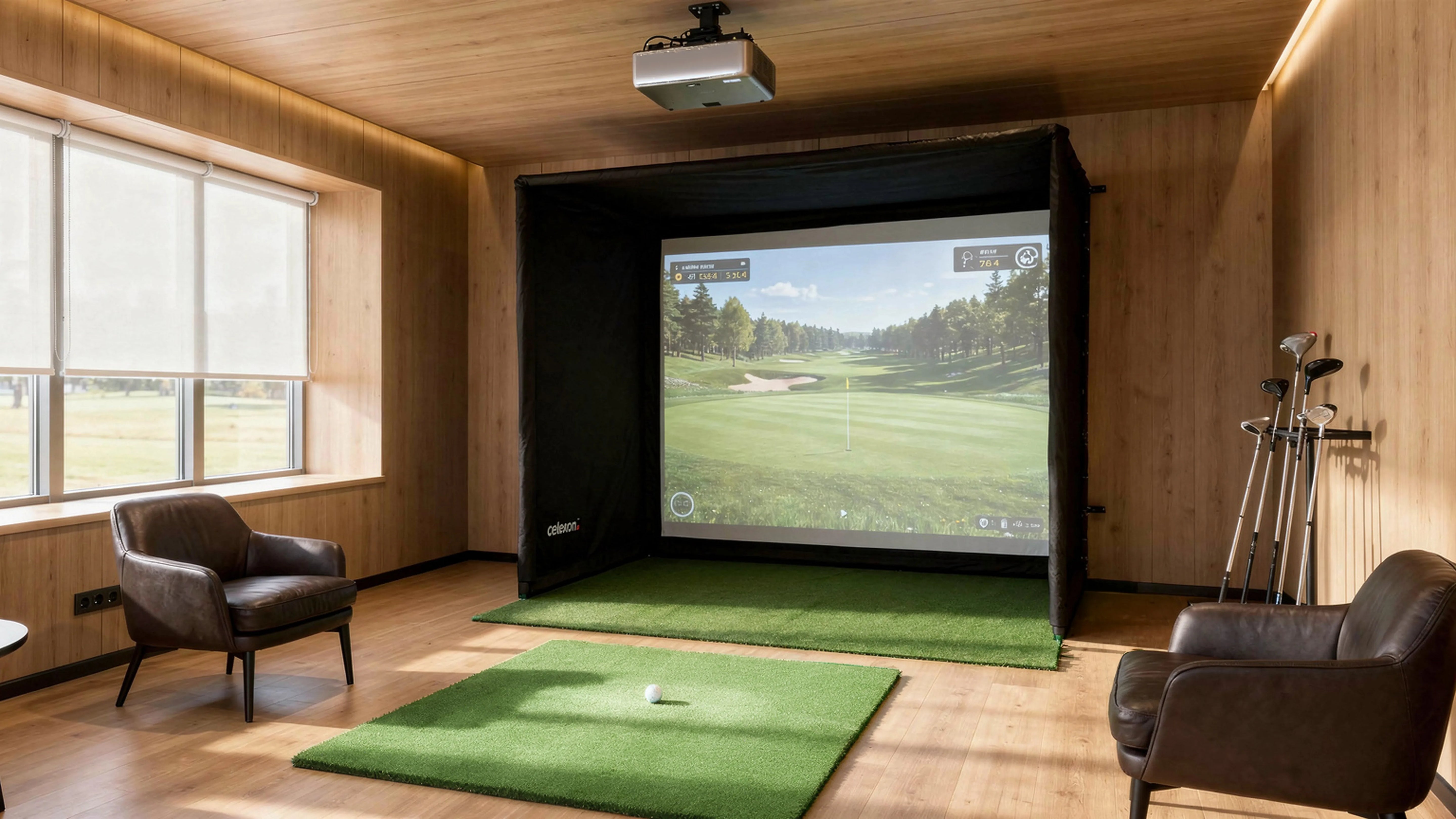 The image shows a stylish indoor golf simulator in a modernly furnished room with warm wood paneling. In front of a large projection screen inside a black simulation enclosure lies an artificial turf mat with a golf ball ready, while a projector mounted on the ceiling projects the virtual golf game onto the screen. Several golf clubs stand next to the setup, and two comfortable leather armchairs as well as large windows with a view outside complete the scene.